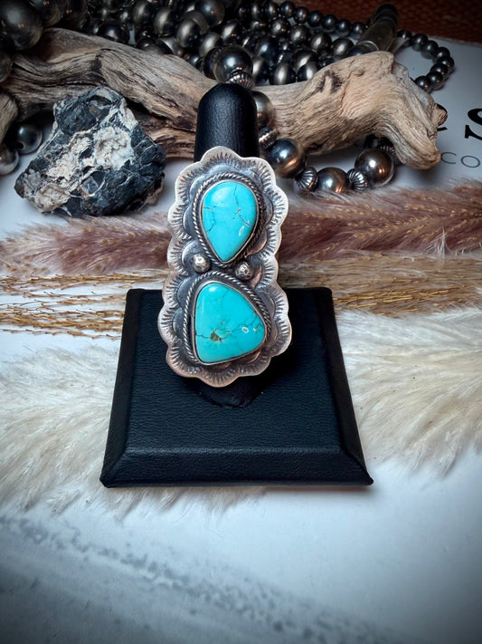 Turquoise ring on a black stand with natural elements in the background